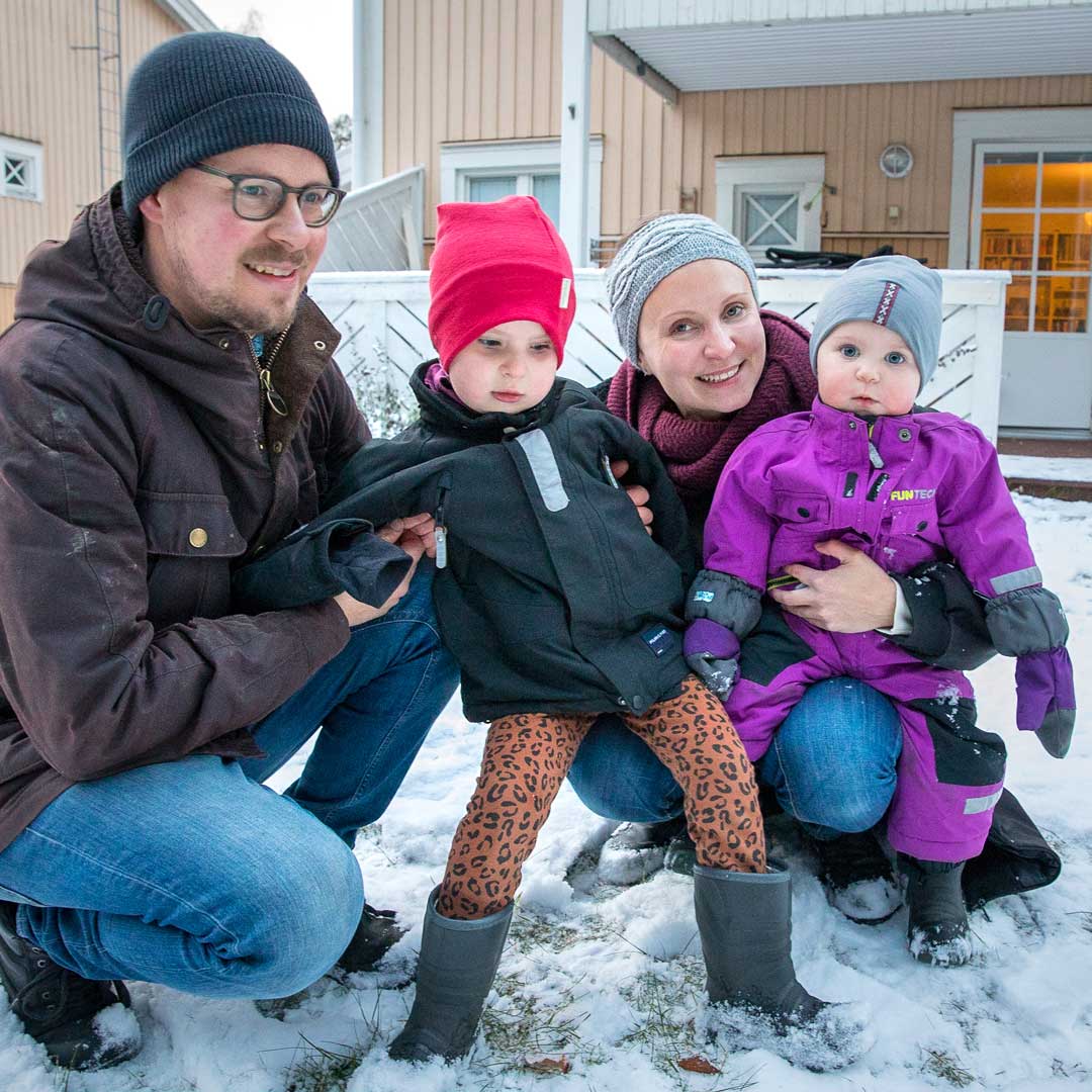 Familj med två vuxna och två barn i trädgården vintertid. Foto.