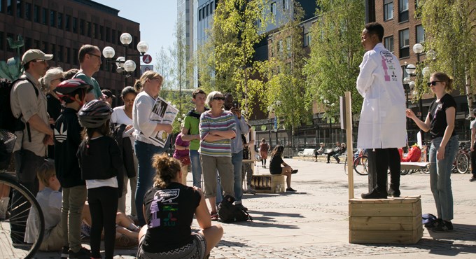 Forskare iförd labbrock pratar inför publik på torget. Foto.