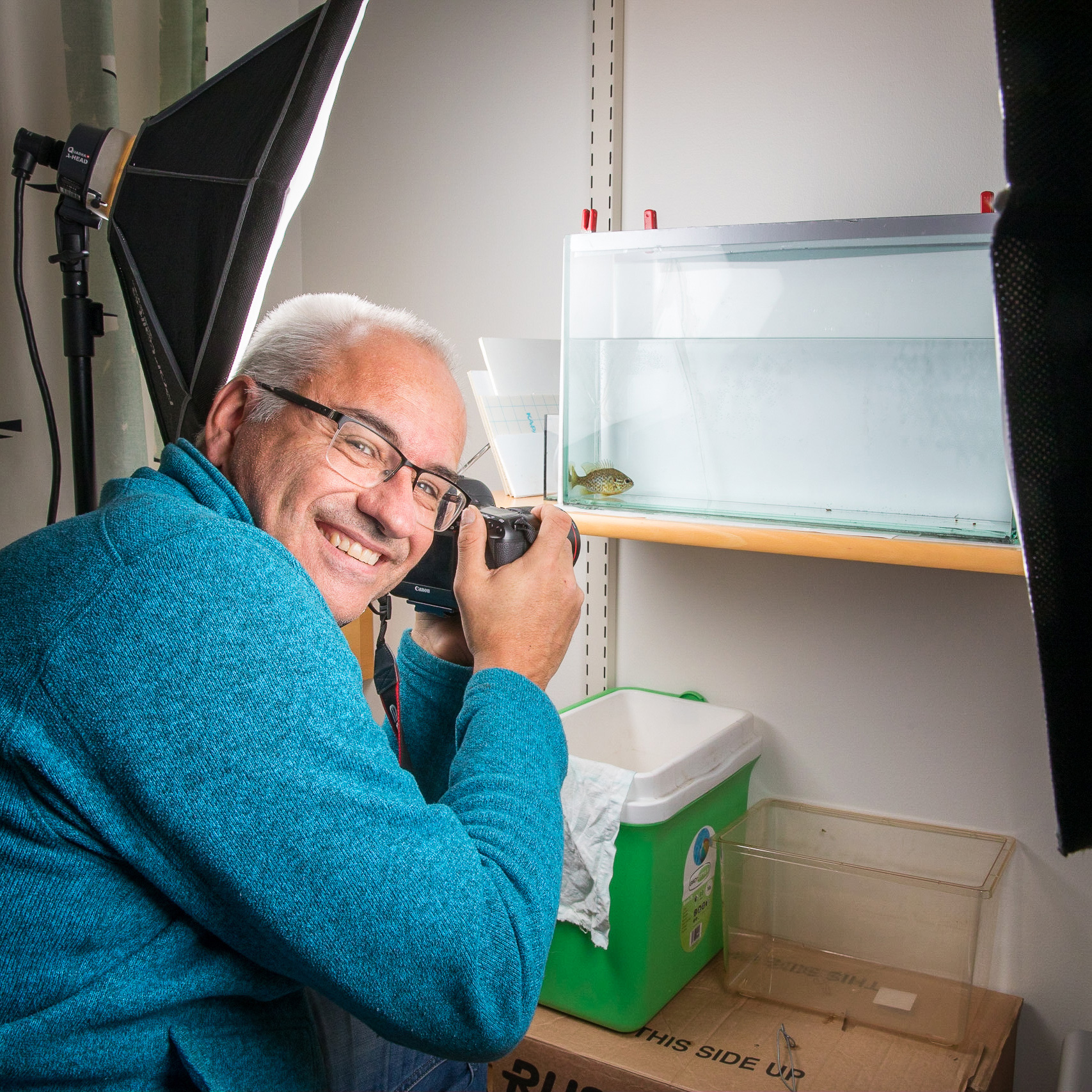 Jörgen Wiklund med kamera och fotoblixtar vid ett akvarium med en fisk i. Foto.