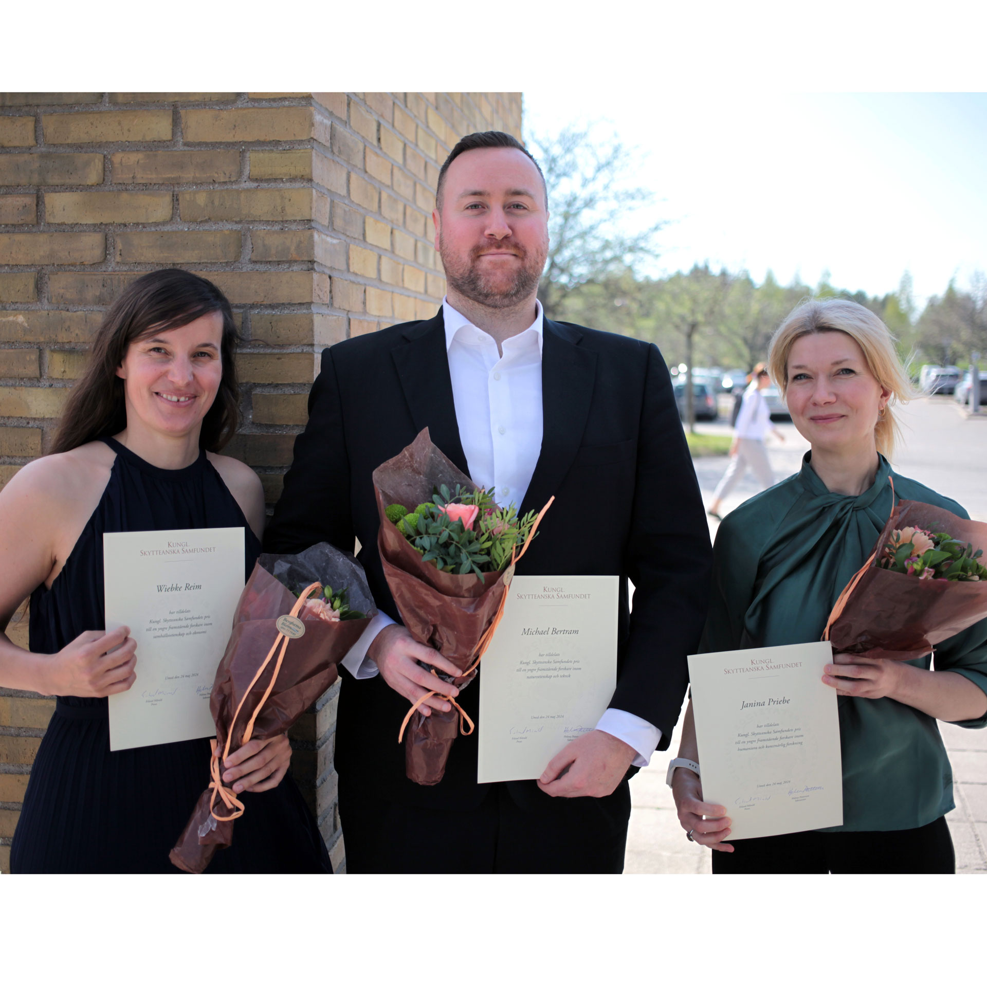 Three winners with flowers and certificates.