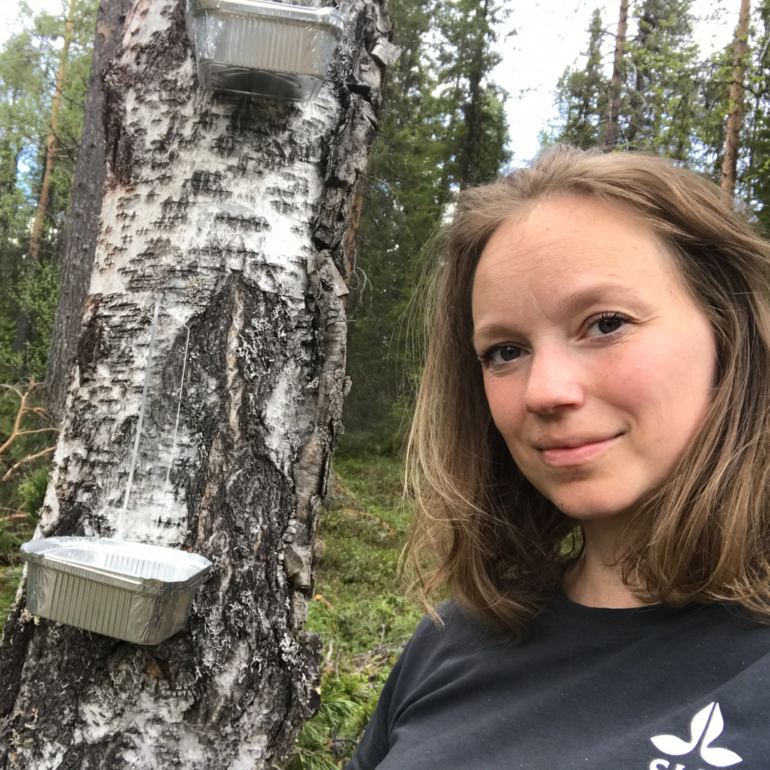 Paulina Bergmark intill en trädstam med två aluminiumbehållare fastsatta.