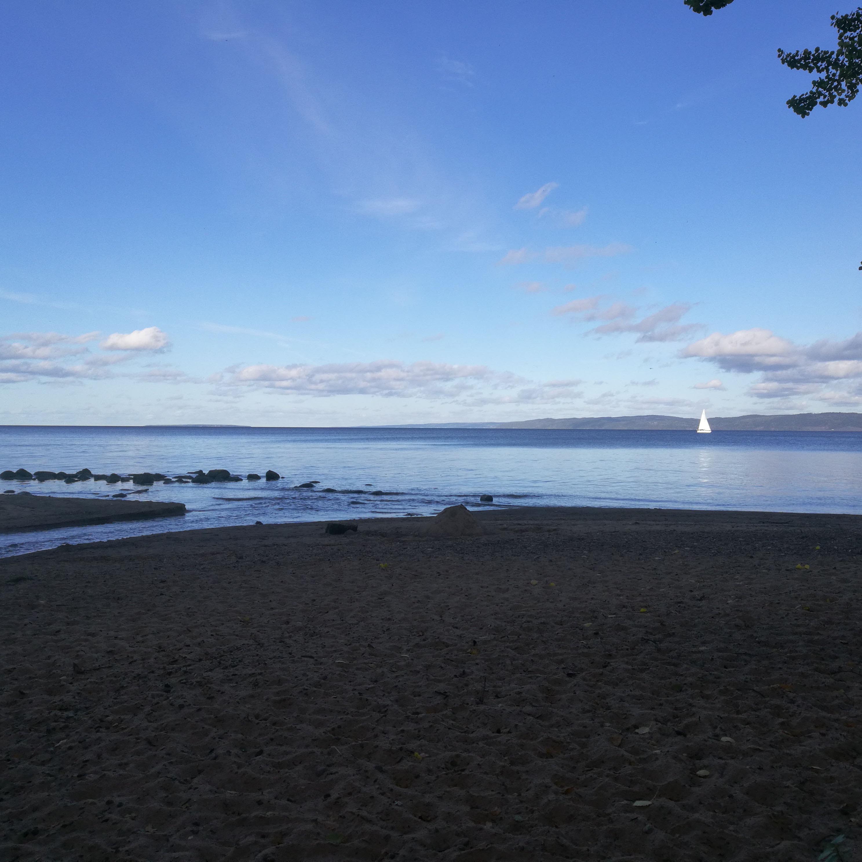 Utsikt mot sjö från strand med utlopp  från vattendrag. Foto.