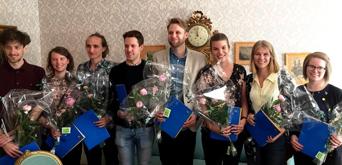 Åtta personer som håller i blombuketter och diplom. Foto.
