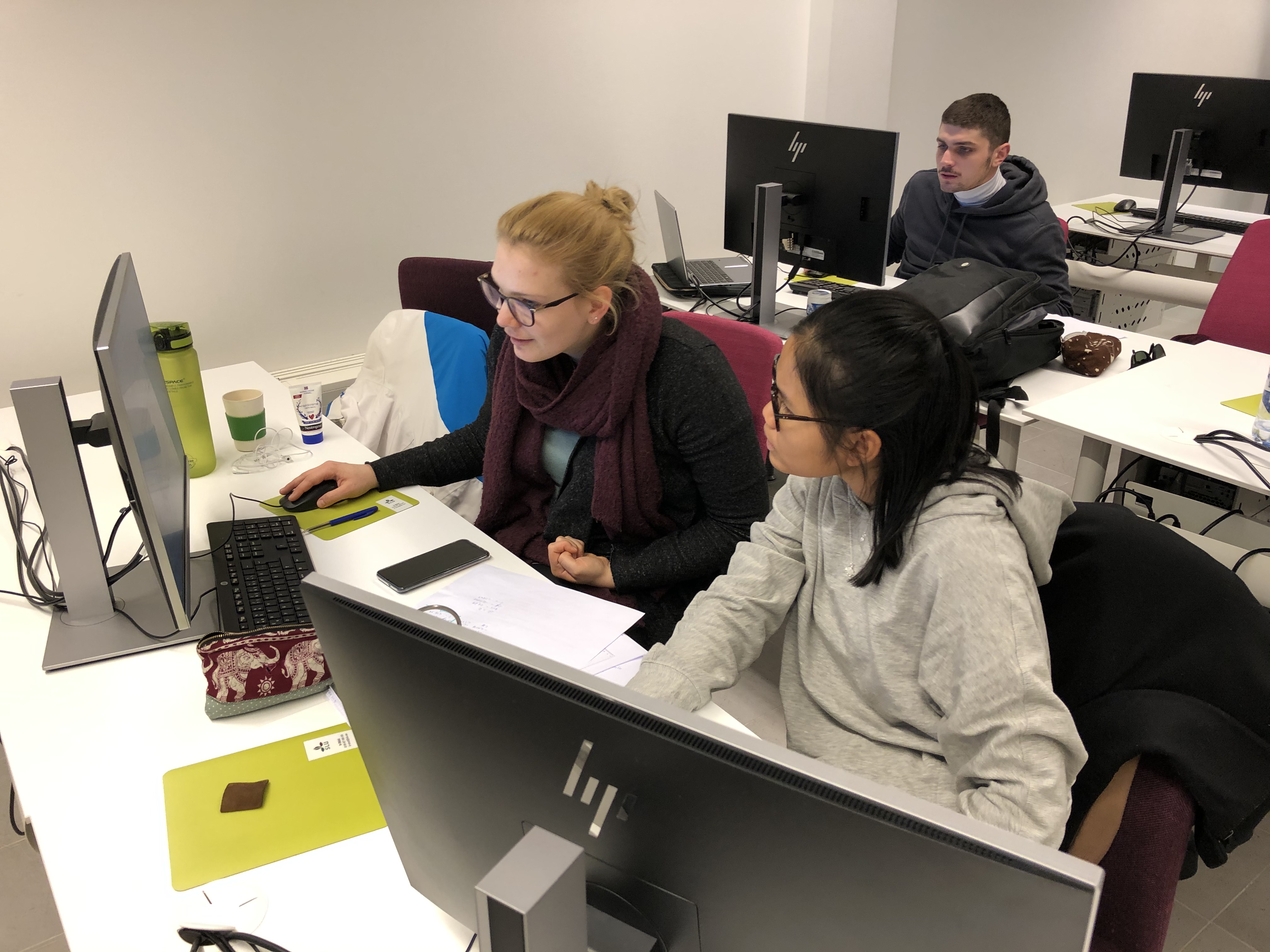 Tre studenter som jobbar i en datorsal, foto.