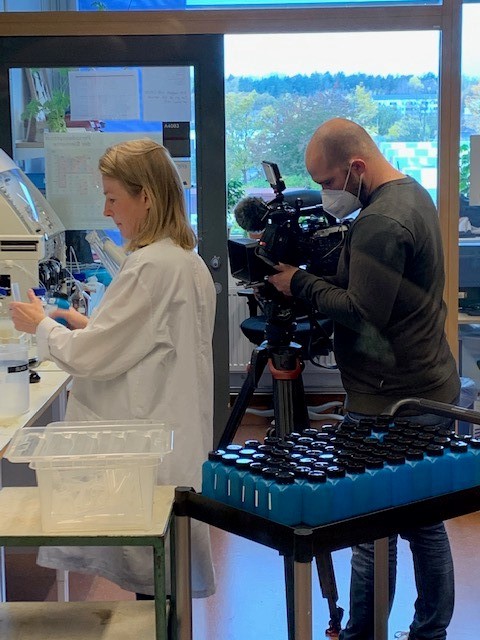 Man som filmar en kvinna som jobbar i ett laboratorium. Foto.