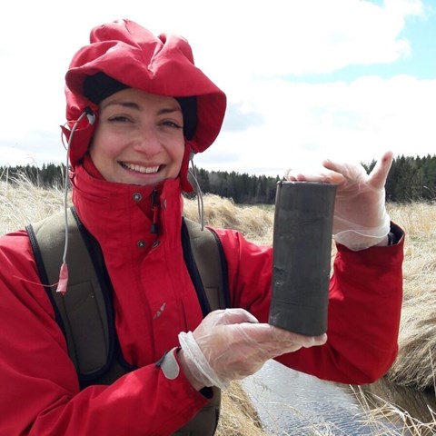 Person som håller ett kompakt sedimentprov framför en bäck. Foto.