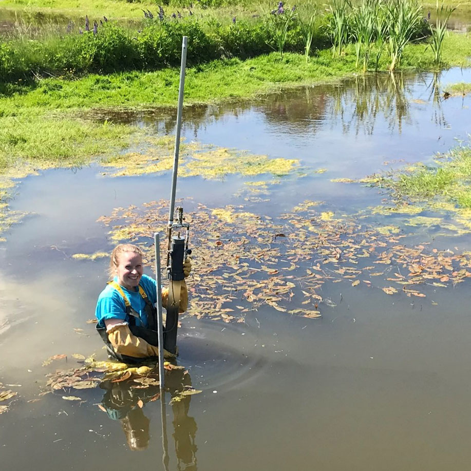 Kvinna står i våtmark med provtagningsutrustning. Foto.