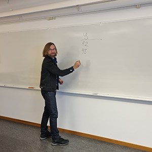 En man skriver siffror på en whiteboard-tavla.
