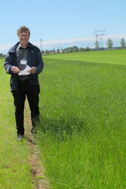 En man står på ett fält med pappersdokument i handen.