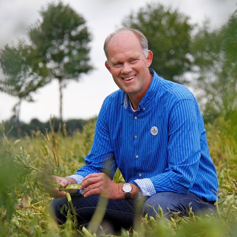 A man in a blue shirt sits on a hillside and smiles.