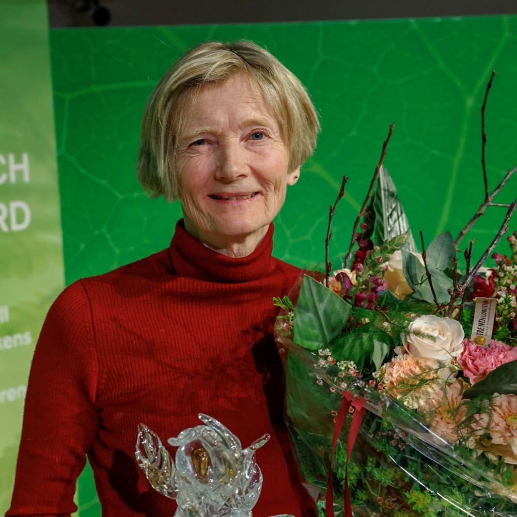 Kvinna med röd tröja håller i en bukett blommor och en prisstatyett. Foto