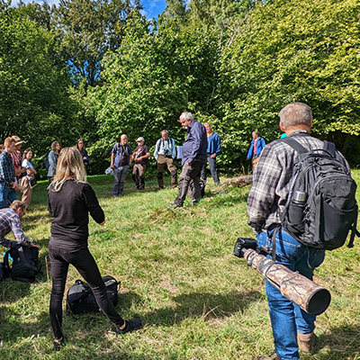Grupp av människor står samlade runt föreläsare i naturen. Foto