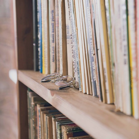 Närbild på en bokhylla med ett par glasögon på kanten av hyllan.