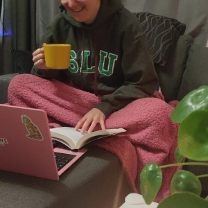 Person sitting with a book in their lap, infront of a laptop computer.