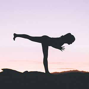 En person står i en yogaposition i motljus.