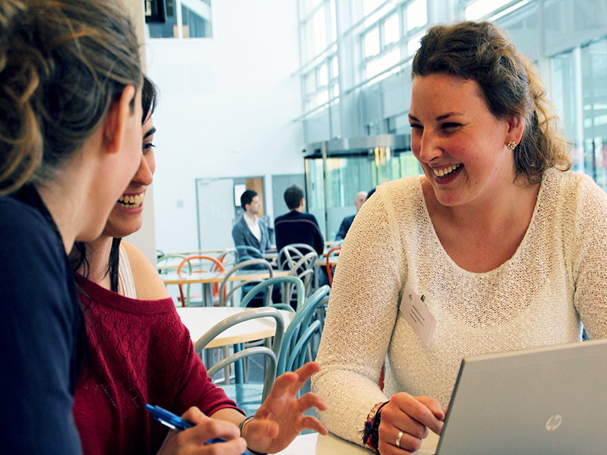 Tre personer sitter vid en dator och skrattar och pratar.