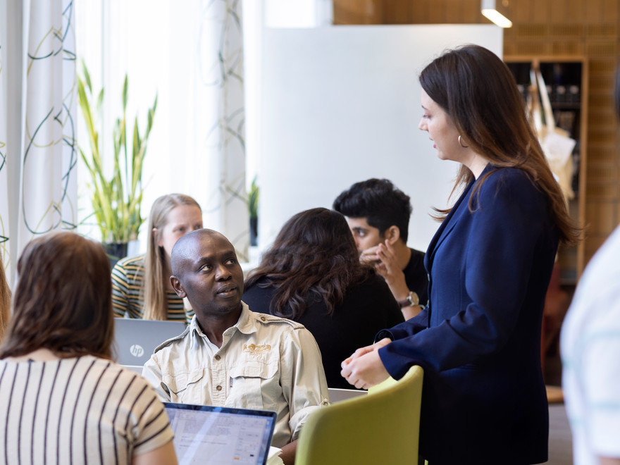 En grupp studenter diskuterar tillsammans, medan en av dem står upp och engagerar sig i samtalet.