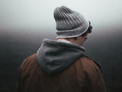 The back of a younger man with a gray hat looks down at the ground. Photo.