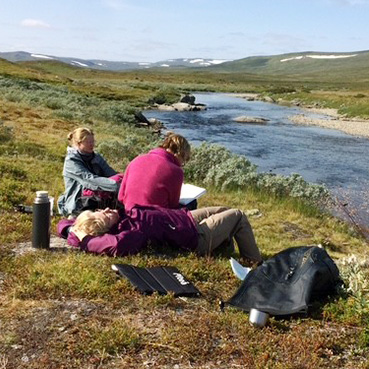 Three people resting by a mountain stream.  Photo.