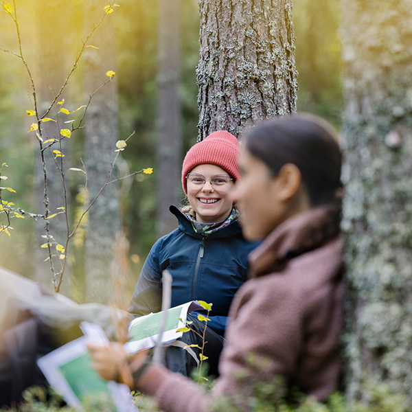 Två studenter i skog. En ler in i kameran. Foto.