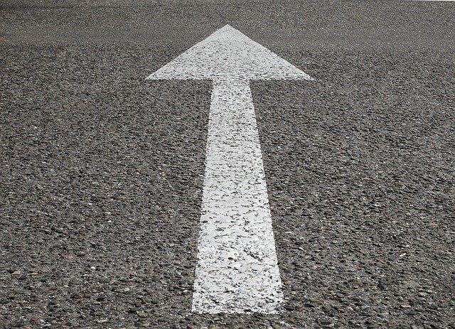 White arrow pointing forward, painted on asphalt. Photo.