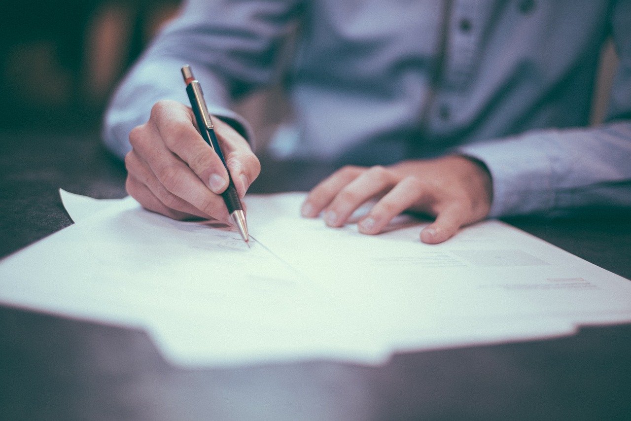  Photo of a man in blue shirt. His hands and arms are visible. The man writes something on a piece of paper.