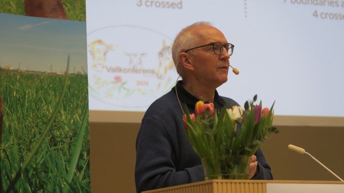 A male person with a headset, with a presentation behind him. 