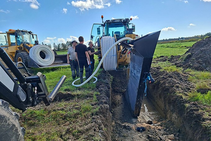 Tre personer står vid stor traktor på en åker. Foto.
