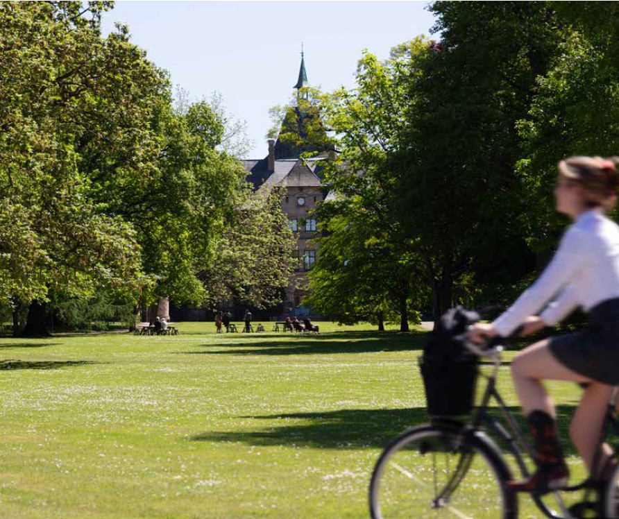 ung kvinna på cykel i en park med slott i bakgrunden