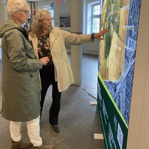Two women in a room pointing at a big map