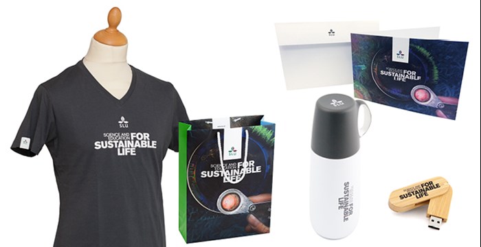 T-shirt with SLU:s brand promise, paper bag with the brand proimse and SLU collage, a white thermos with brand promise in grey and a a  grey mug with white SLU logo. A card with SLU logo and brand promise, and a usb stick in bamboo with the brand promise. Photo.