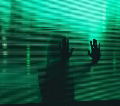  Silhouette of a person pressing hands against a green pane of glass. Photo.