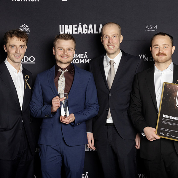 Fyra personer i bredd, en med ett diplom i handen. Foto.