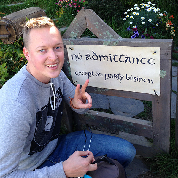 Man som sitter ner och pekar på en skylt på en trädgårdsgrind. Foto. 