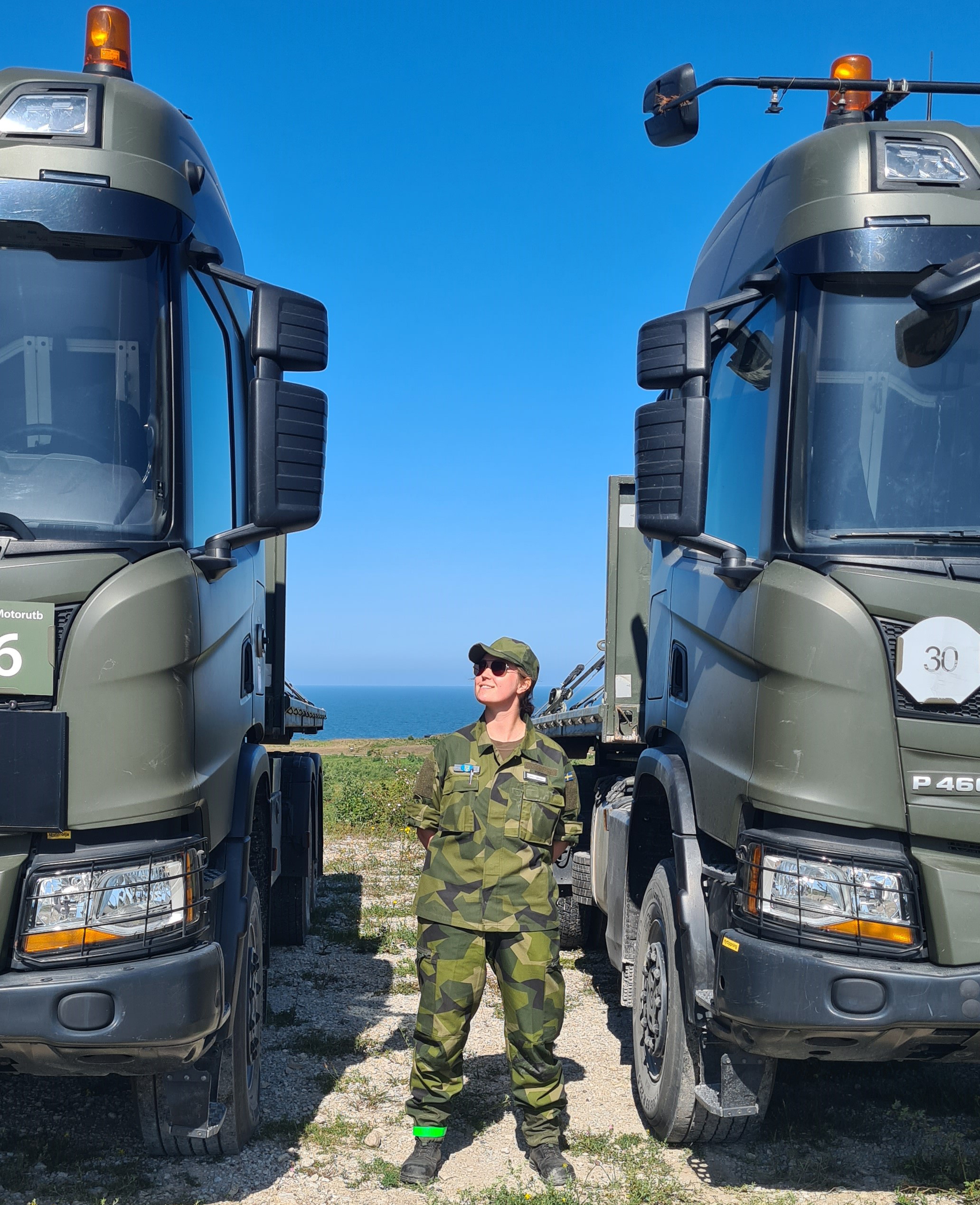 Kvinna i uniform mellan två gröna lastbilar