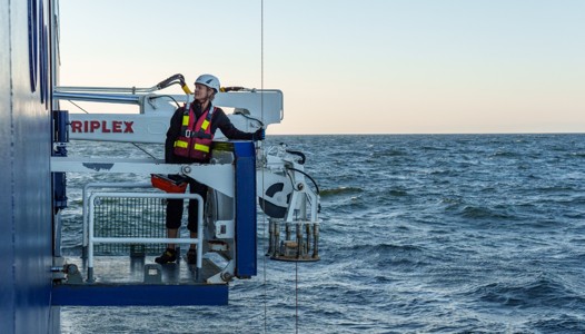 En person i skyddsutrustning står på en plattform ovanför havet.