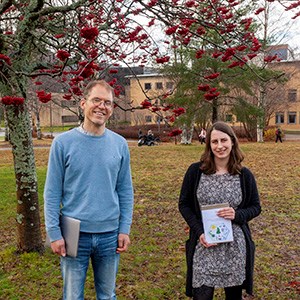 Anne Bünder standing outside on the right side of the picture with her thesis in her hand togehter with her supervisor Totte Niittylä on the left side