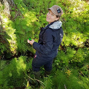 Kvinna i skogen tittar in i kamera.