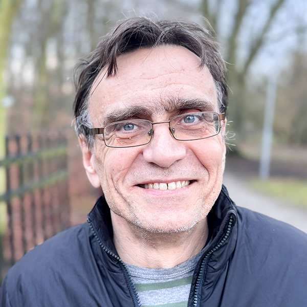 En man i glasögon ler in i kameran. Foto.