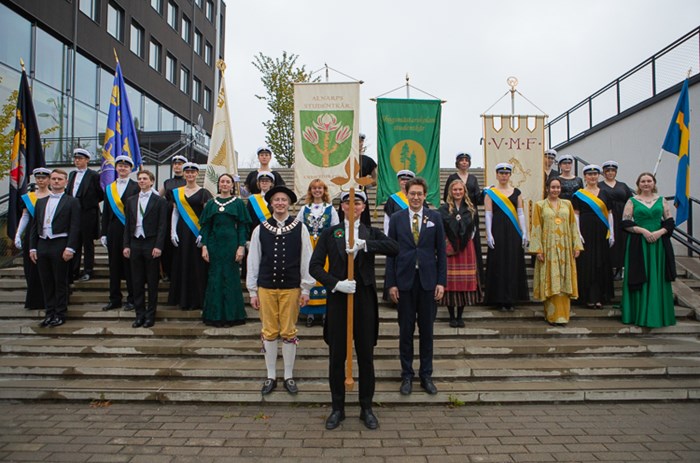 A group of students wearing festive dresses and student caps. Some of them holding banners.