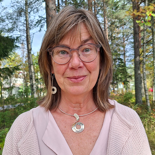Kvinna i glasögon och stort silverhalsband ler mot kameran.