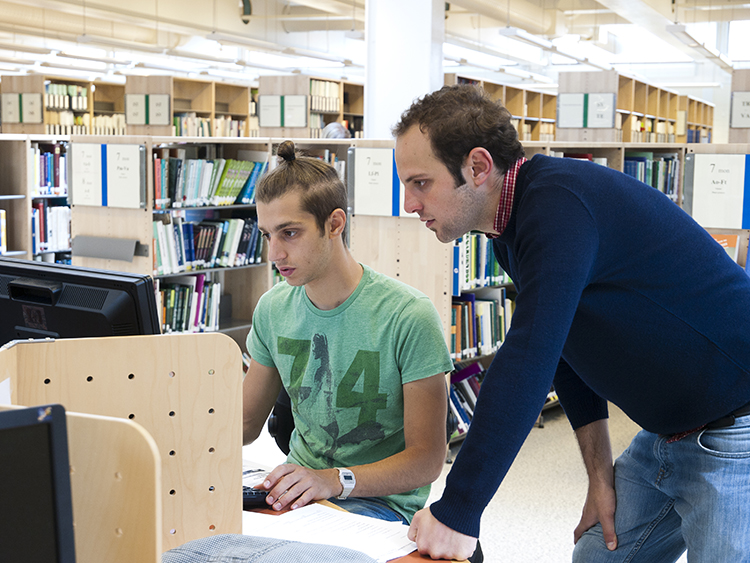 Två studenter framför en dator i biblioteket, foto.