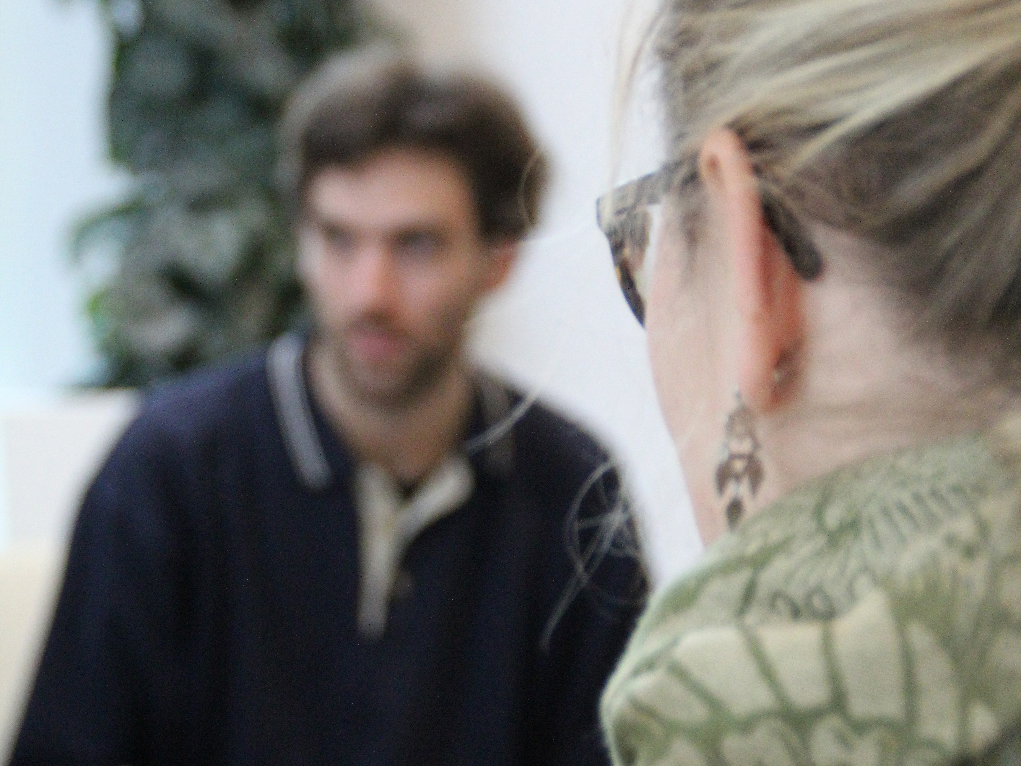 Två personer sitter mitt emot vasrandra och samtalar, foto.